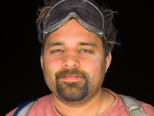 A man with goggles smiling. He is wearing a t-shirt with a triangle and circle fractal pattern. He is dusty because the picture was taken by Aaron Dressin at Burning Man. The man is the author of this webpage. He is me.
